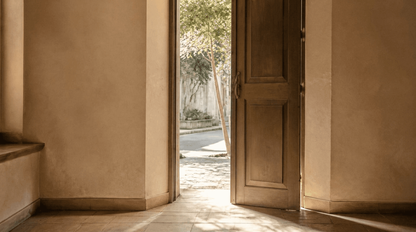 An open door in a quiet room, daylight and a tree beyond it