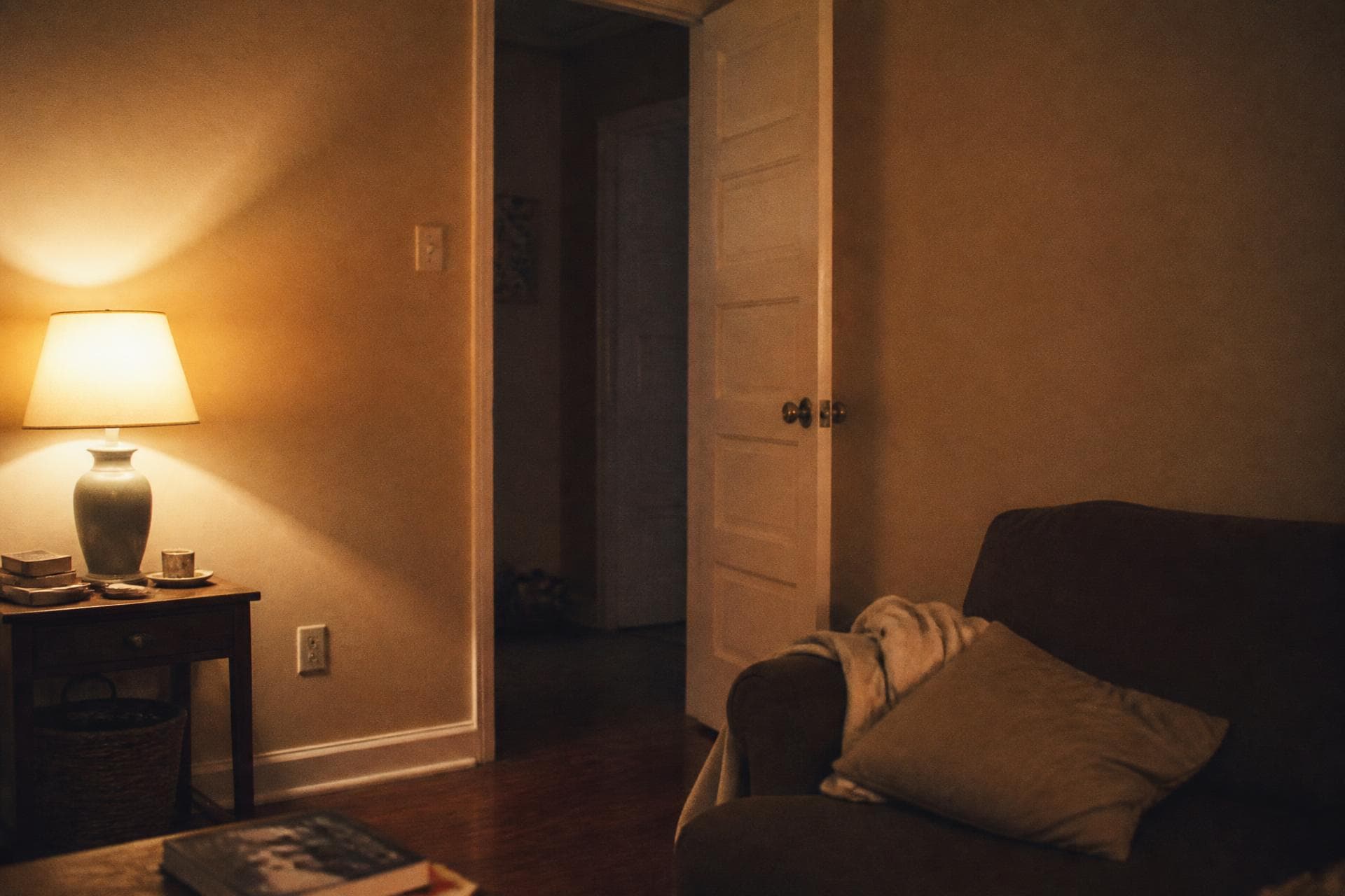 A room in the evening with one lamp left on and a door half open